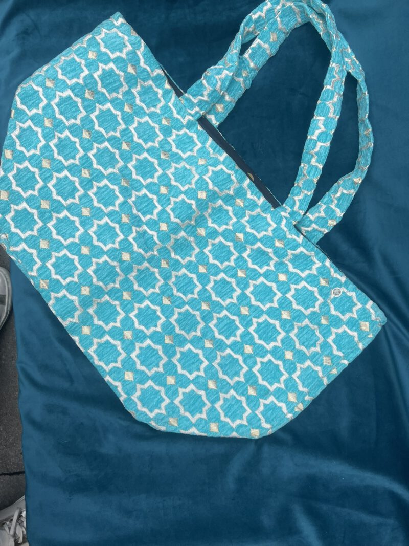 Zahra Turquoise– Handgefertigte Brokattasche in intensivem Türkisblau mit weiß-goldenem Muster, fotografiert auf blauem Samt, Boho Nomad Collection