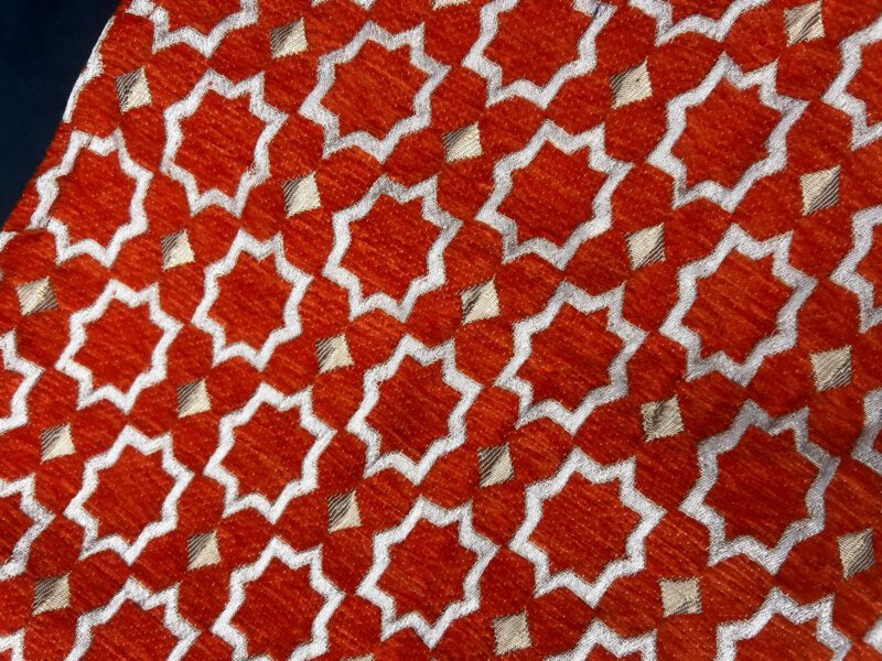 Detailansicht der Brokatstruktur von Boho Nomad Grand – Zahra Sahara, dunkles Orange mit weiß-goldenem Muster, handgefertigt in Marokko