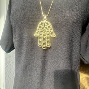 Goldene Kette mit filigraner Hamsa-Hand als Anhänger, getragen auf dunklem Shirt