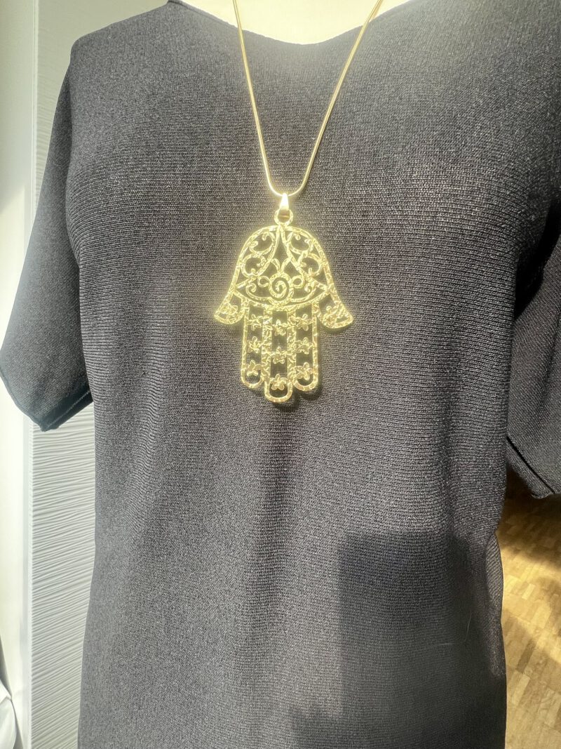 Goldene Kette mit filigraner Hamsa-Hand als Anhänger, getragen auf dunklem Shirt